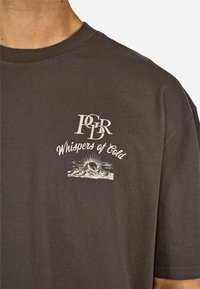 Tmavošedé bavlnené tričko s okrúhlym výstrihom, s bielym grafickým textom "Whispers of Cold" a ilustráciou hory na ľavej strane.