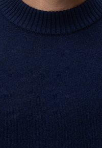 Gros plan sur le col d'un pull en maille bleu marine montrant un col côtelé et un tissu texturé.