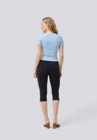 Šviesiai mėlynas trumpomis rankovėmis marškinėliai su raukšlėtu paviršiumi, derinami su juodais capri tipo leggingais. Modelis dėvi atviras smėlio spalvos blokines kulniukus.