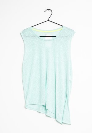 Jasnoniebieska bluzka bez rękawów z subtelnym wzorem, okrągłym dekoltem i asymetrycznym dołem, wisząca na czarnym wieszaku na białym tle.