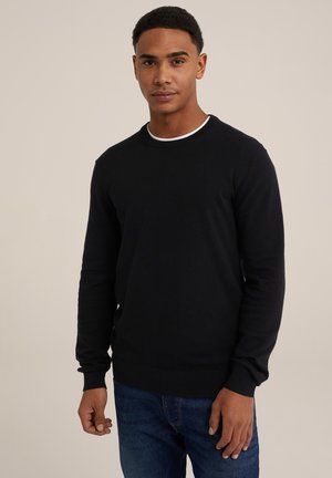 Black crew-neck sweater with long sleeves, ribbed cuffs and hem, featuring a white accent at the neckline. Worn with blue jeans.