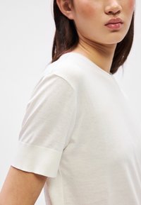 Camiseta blanca de manga corta con cuello redondo clásico. Fabricada en algodón suave y liso, con textura acanalada en los dobladillos de las mangas. Diseño minimalista.