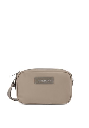 Sac bandoulière rectangulaire beige avec fermeture éclair sur le dessus, sangle ajustable et patch logo "Lancaster Paris" cousu à l'avant.