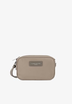 Sac bandoulière rectangulaire beige avec fermeture éclair sur le dessus, sangle ajustable et patch logo "Lancaster Paris" cousu à l'avant.