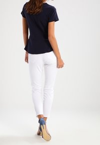 Marinblå peplumtop i kombination med vita slim-fit jeans och blå högklackade skor. Slät väv med korta ärmar och en figursydd silhuett.