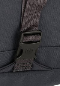 Correa de tela negra con superficie texturizada, que presenta una hebilla de plástico gris con un logo, adjunta a un fondo de tela oscura.