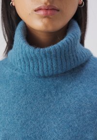 Pull col roulé bleu clair en tissu tricoté doux et texturé. Doté d'un col côtelé et d'une coupe confortable et décontractée.