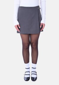 Gonna mini grigia con design plissettato e dettagli in metallo argentato, abbinata a scarpe nere in vernice, calzini bianchi e collant neri trasparenti.