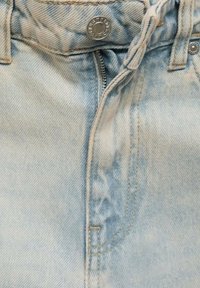 Vaqueros de denim azul claro con una cremallera tradicional, cierre de botón metálico y costuras en contraste a lo largo de las costuras.