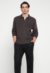 Rudas megztinis su apykakle, trimis sagomis ir rib onuotos rankogaliais. Derinamas su juodomis kelnėmis, kurios turi mažą žymelę apačioje.