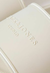 Récipient rectangulaire de couleur crème avec le texte « SACK & JONES studio » en relief sur la surface.