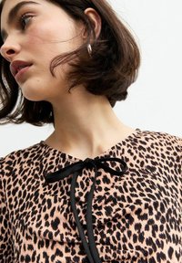 Leopardenmuster-Bluse in Beige- und Schwarztönen, mit einem schwarzen Band zum Binden am Ausschnitt und strukturiertem Stoff.