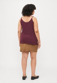 Burgundy sleeveless top with textured fabric, paired with a brown mini skirt. Model wearing black flats, viewed from the back.