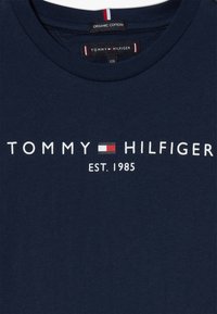 Camiseta de algodón orgánico azul marino con el logotipo de Tommy Hilfiger, bandera en rojo, blanco y negro, y "EST. 1985" impreso en el frontal.