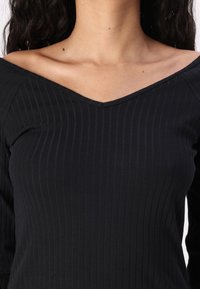 Black ribbed top with a v-neckline and long sleeves, featuring a textured fabric that highlights the fitted silhouette.