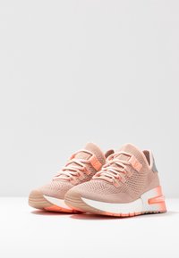 Ljusrosa sportskor med ovandel i stickad textil, strukturerade detaljer, dämpad sula och vit mellansula. Har orangea accenter.