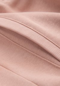 Zacht roze stof met een close-up van geribbelde en gladde gebreide texturen en zichtbare naden op gevouwen materiaal.