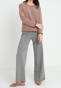 Czerwony i biały sweter w dzianinę z szerokim dekoltem, zestawiony z szarymi spodniami o szerokich nogawkach w jodełkę oraz płaskimi butami.