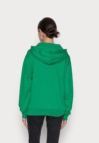 Sudadera verde fabricada con material suave; presenta una capucha espaciosa y mangas largas, con puños y dobladillo de canalé para un ajuste relajado.