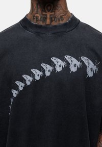 Zwarte katoenen t-shirt met een graphic van tien witte vlinders in een gebogen formatie over de borst, met een verstevigde halslijn.