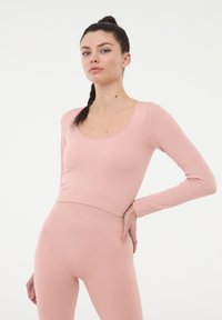 Jasnoróżowa bluzka z długim rękawem, okrągłym dekoltem i żeberkowaną fakturą, połączona z pasującymi, żeberkowanymi legginsami o wysokim stanie.