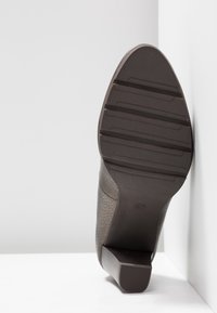 Chaussure à talon marron avec une tige en cuir texturé et une semelle en caoutchouc. Le talon est de forme bloc et la semelle extérieure présente des rainures horizontales pour une meilleure adhérence.
