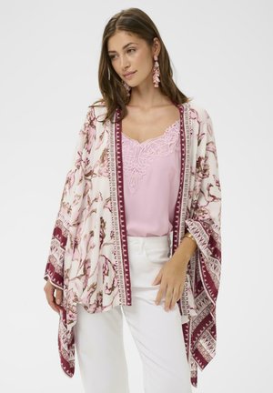 Blomstret kimono i lyserød med mørkerøde detaljer, med åbne ærmer og mønstret kant; lagdelt over en pink blondebesat top og hvide bukser.