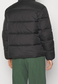 Svart puffjacka med en boxig passform, quiltat mönster, ribbade ärmslut och hög krage. Slät, matt yta utan synlig märkning.