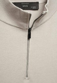 Beiger Halbreißverschluss-Pullover mit geripptem Kragen und subtiler Textur. Verfügt über einen Frontreißverschluss mit schwarzem Zugband und Etikett innen.
