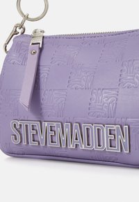 Porte-monnaie en lavande de Steve Madden avec motif SM en relief, fermeture éclair argentée, tirette en cuir et clip porte-clés attaché.