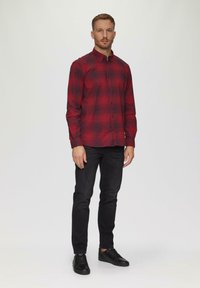 Rood en zwart geruiten shirt met knoopsluiting, lange mouwen en een slim fit, gecombineerd met zwarte jeans en zwarte schoenen.