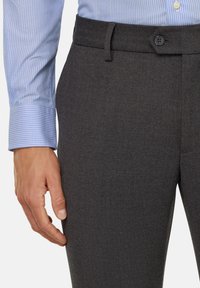 Pelēki vilnas bikses ar gludu tekstūru, ar jostu, kurā ir viena poga, un sānu kabatām. Saskaņotas ar gaiši zilu svītrainu krekliņu.