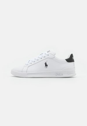 Hvite sneakers laget av syntetisk materiale med en teksturert gummisåle, med en svart aksent på hælen og en brodert logo på siden.