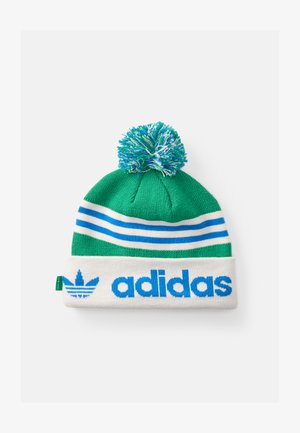 Zaļš adīts beanie ar baltu maliņu, ziliem svītrainēm un zilo "adidas" logo. Vāciņa augšpusē ir daudzkrāsains pūkains cimds.