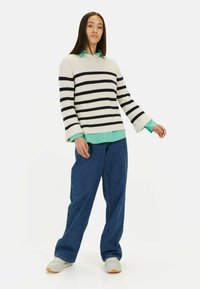 Sweter w paski w kolorze kremowym i granatowym z ryżowym wzorem, nałożony na miętową bluzkę. W zestawie z szerokimi dżinsami i sneakersami.