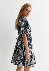 Vestido de color navy con patrón abstracto en blanco, mangas cortas abullonadas, cintura ajustada y dobladillo con volantes en capas. Fabricado en una tela ligera.