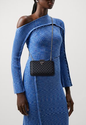 Borsa a tracolla intrecciata nera con tracolla in catena argentata, indossata sopra un vestito blu a coste con texture, caratterizzato da un design off-the-shoulder e dettagli con bottoni.