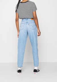 Ljusblå hög midja jeans med raka ben, tillsammans med en svart och vit randig kort t-shirt. Mörka skor med vita sulor.