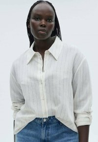 Hvidstribet skjorte med knapper lavet af letvægtsstof, med klassisk krave og optrukne ærmer, parret med blå denimjeans.