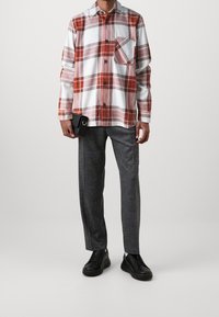 Červená a bílá kostkovaná košile s náprsní kapsou, spárovaná s tmavě šedými, přizpůsobenými kalhotami a černými teniskami. Jednoduchý design a jednobarevné odstíny.