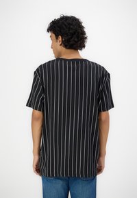 Svart kortermet t-skjorte med hvite vertikale striper, rund hals og løs passform, sammen med blå denimjeans.