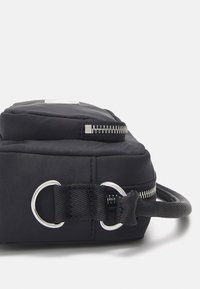 Czarna torba o smukłym, prostokątnym kształcie, z teksturowanym paskiem, srebrnymi akcentami i gładkim zapięciem na zamek u góry.