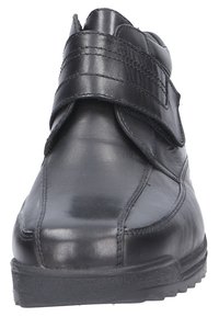 Schwarzer Lederschuh mit Klettverschluss und genähten Details, ausgestattet mit einer robusten Gummisohle und einem runden Zehendesign.