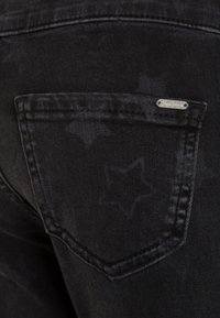 Svarta denimjeans med ett stjärnmönster tryckt på tyget. Inkluderar en liten metalltagg med varumärket på bakfickan.