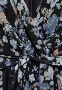 Vestido envolvente floral con una base negra y patrones de flores en azul, rosa pálido y blanco, tejido texturizado y detalle de cinturón atado.