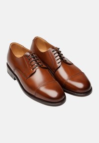 Braune Leder-Dressschuhe mit glänzender Oberfläche, ausgestattet mit einer Kappenzehe, Schnürdesign und einer abgerundeten Schuhspitze. Glatte Textur und minimale Akzente.