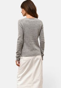 Szary sweter dzianinowy z długimi rękawami, okrągłym dekoltem i ściągaczami, zestawiony z białą spódnicą dżinsową z tylnymi kieszeniami i prostym krojem.