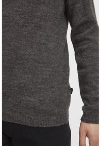 Grauer Strickpullover aus weicher Wolle mit strukturierter Oberfläche, mit gerippten Bündchen und Saum sowie einem kleinen Markenetikett an der Seite.