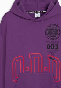 Felpa viola con un grande logo rosso "O.D.D." sul davanti, una tasca a marsupio e elementi di branding vicino al collo.