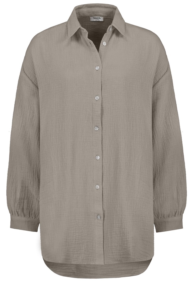 Long-sleeve, button-up shirt in light taupe, featuring a textured fabric, a classic collar, and a curved hemline with slight gathers at the cuffs.
